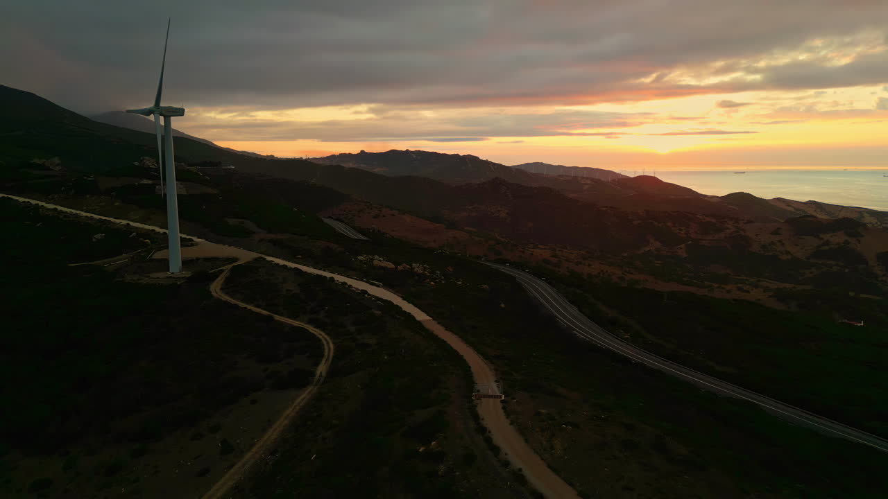 descenso del avión no tripulado durante el atardecer con el molino de viento a lo largo de la costa de españa