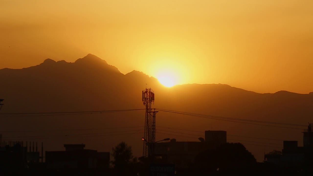 puesta de sol en las montañas cerca de una ciudad, vista de silueta con una torre satelital, casas y edificios, ángulo bajo