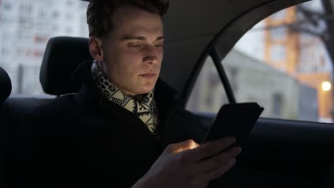 Attractive-Young-Sexy-Guy-In-Stylish-Black-Trench-Coat-Riding-In-A-Car-Looking-At-His-Smartphone