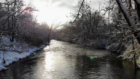 aerial sunrise shot of creek in winter forest in michigan, usa