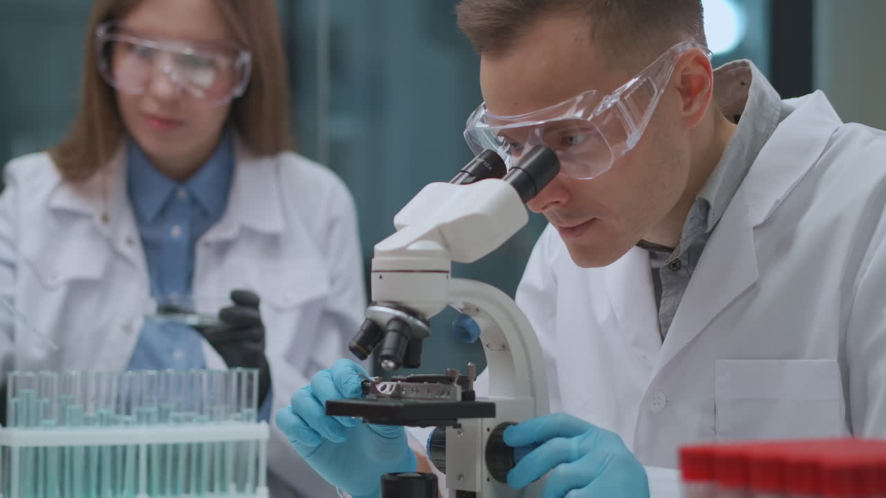un par de científicos está trabajando en un laboratorio de crimen. un hombre está viendo pruebas en el microscopio. una mujer está probando líquidos en tubos de ensayo.