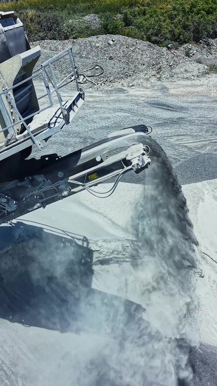 Attrezzature per cava di granito lavorano la pietra in un sito di giorno con la polvere che si alza dal pavimento della cava e una macchina al lavoro.