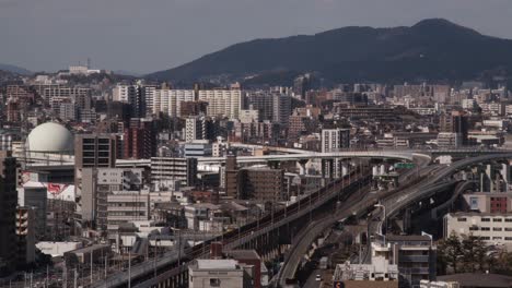 wide of shinkanzen bullet train moving through japanese cityscape, kokura, kitakyushu, japan with mountains and river