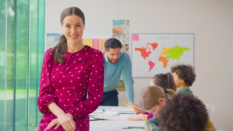 retrato de una maestra de escuela primaria sonriente trabajando en un escritorio en el aula con estudiantes