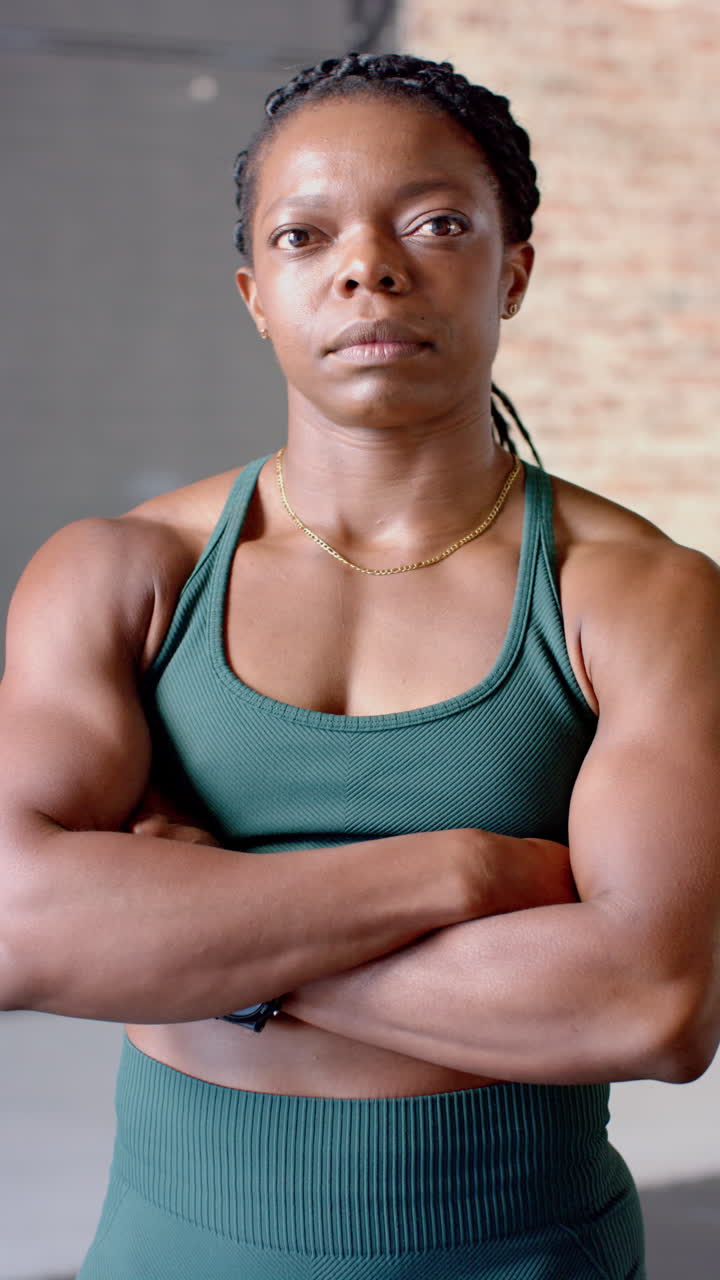 Vertical video: Confident woman in gym wearing sportswear, crossing arms and looking determined