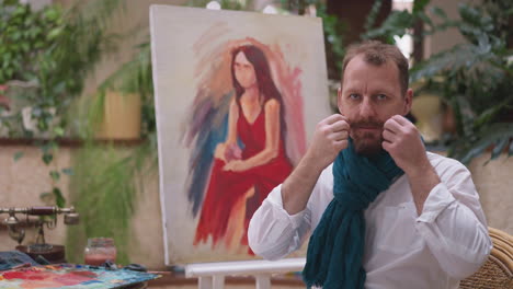 man painter adjusts curled mustache with care. artist adds layer of authenticity to artistic process sitting against woman portrait in modern art studio