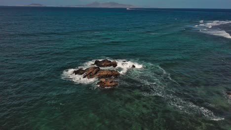 Olas-Rompiendo-En-Las-Rocas-Frente-A-La-Costa-De-Corralejo,-Islas-Canarias,-Día-Despejado,-Vista-Aérea