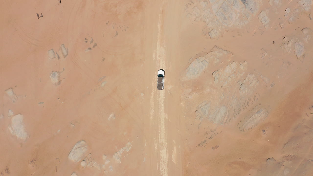Top down drone shot of a white car traveling a remote gravel road in Namibia’s desert