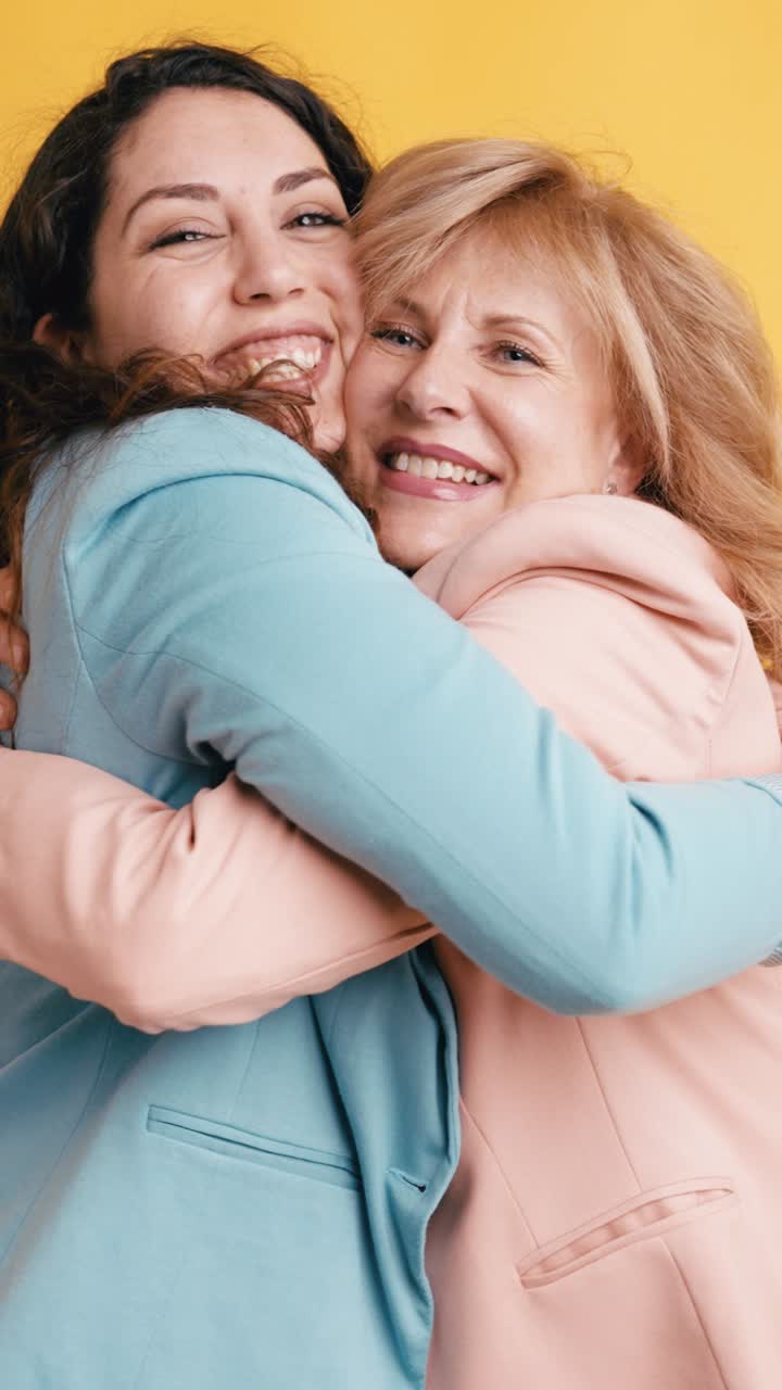 Due donne felici che si abbracciano e sorridono su sfondo giallo