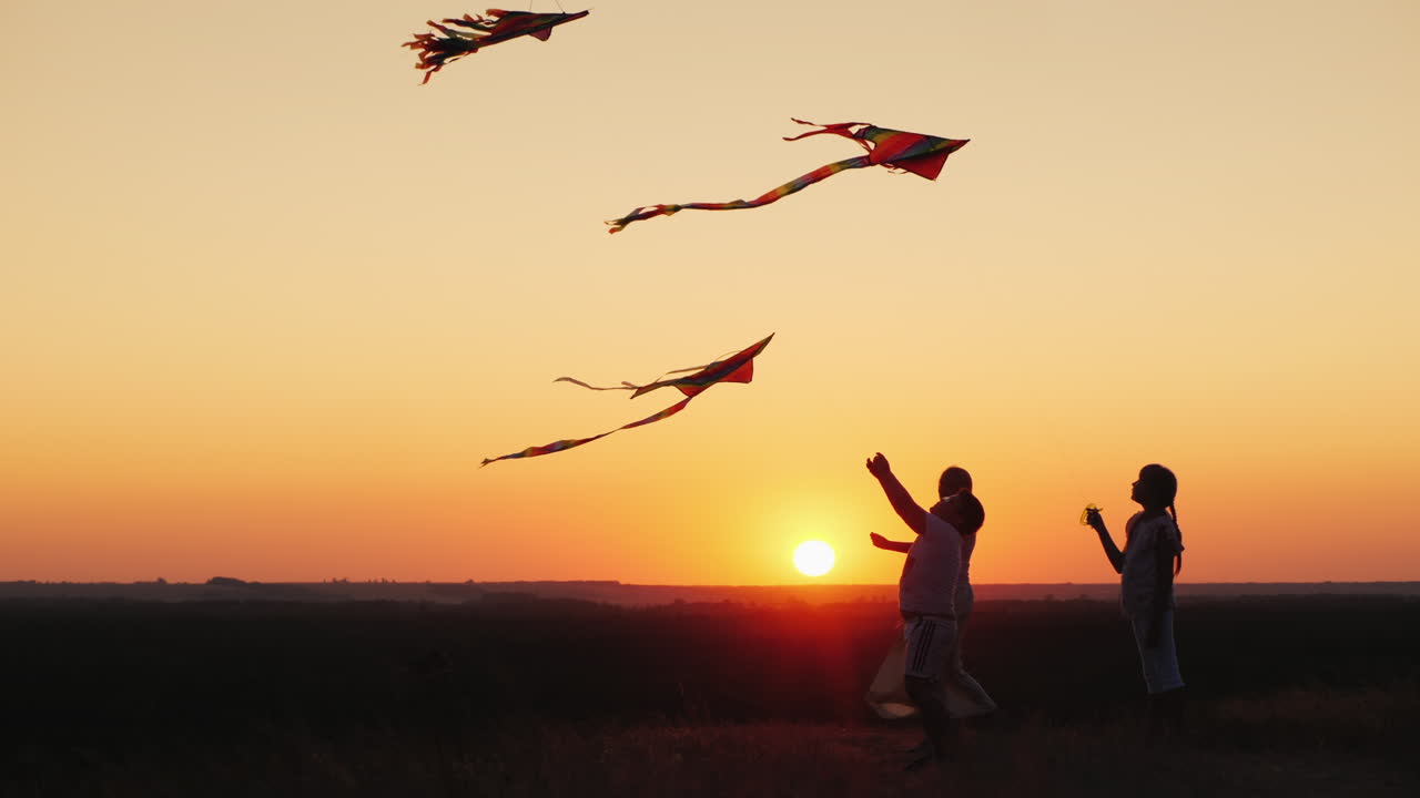 los niños con mamá juegan una cometa al atardecer en una noche de verano padres e hijos activos