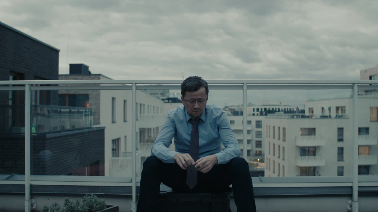 A sad man in a shirt smokes a cigarette on the balcony