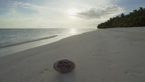 A-Beach-scene-of-the-Indian-Ocean-in-the-Maldives-after-Sunrise-with-a-Do-not-disturb-carved-Coconut-on-the-sand