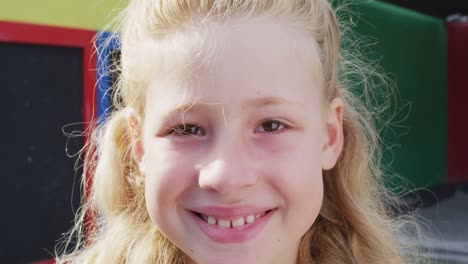 portrait of happy caucasian schoolgirl looking at camera on playground