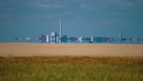 the contrast between nature and industry - a yellow wheat field and an industrial plant in the background on the danish coast