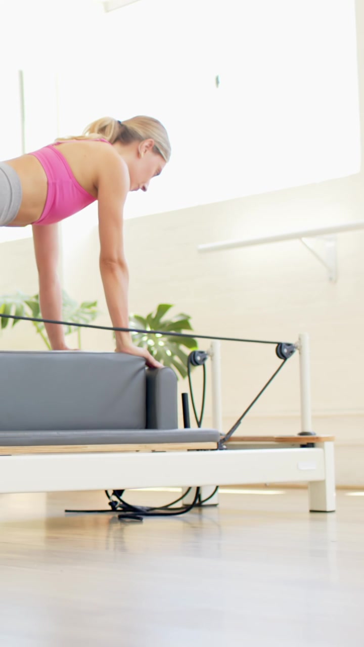 Donna che inizia in plank alto sul reformer, spostando il peso e regolando il carrello per il core di pilates.
