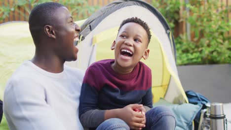 video of happy african american father and son playing in tent in garden