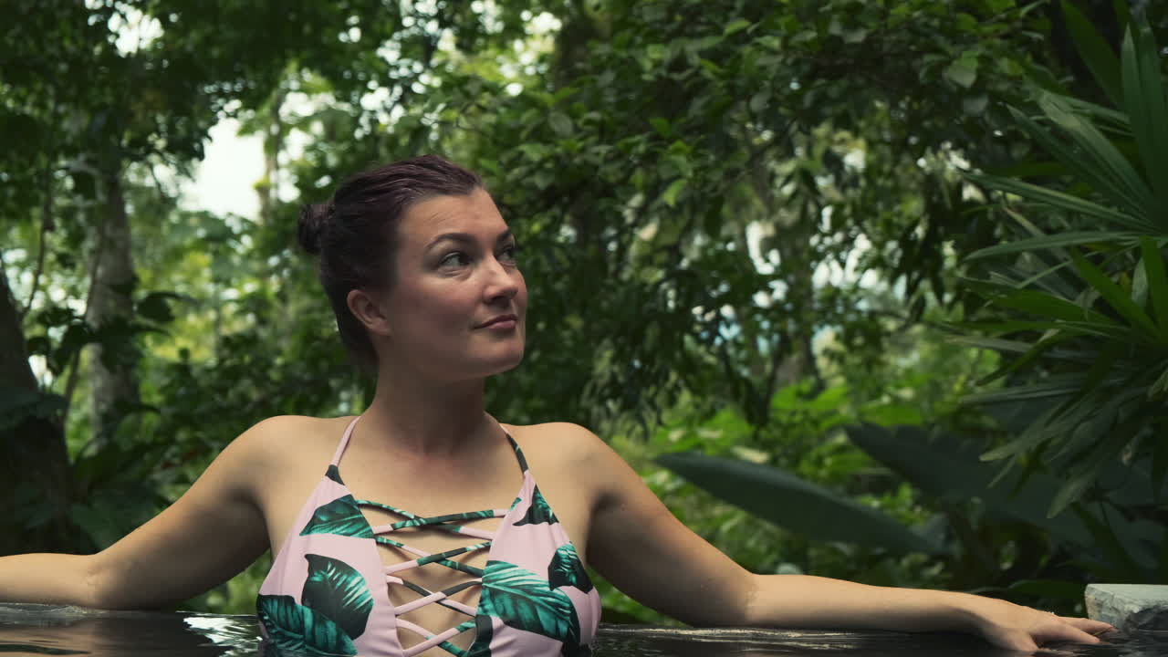 온천수에서 수영복을 입은 젊은 여성에게 자연 환경을 바라보며 몸을 기울이십시오.