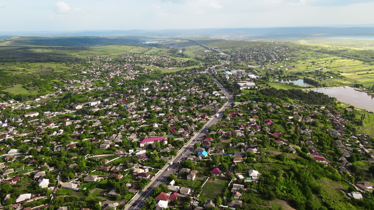 Aerial drone view of a village and road with cars, greenery, hills and lake, Moldova