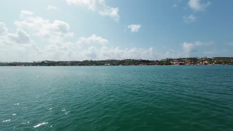 Slow-motion-action-camera-shot-from-the-tropical-Restinga-beach-on-a-large-crystal-clear-turquoise-river-across-from-the-coastal-town-of-Barra-do-Cunhaú-in-Rio-Grande-do-Norte,-Brazil-on-a-summer-day