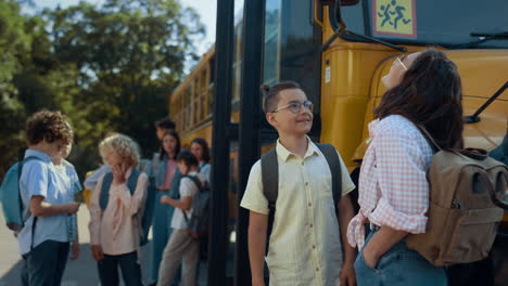 two pupils stand chatting at schoolbus waiting bus boarding. friends talking.