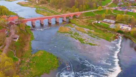 Widest-waterfall-in-Europe---Venta-Rapid,-aerial-tilt-up-towards-arch-bridge