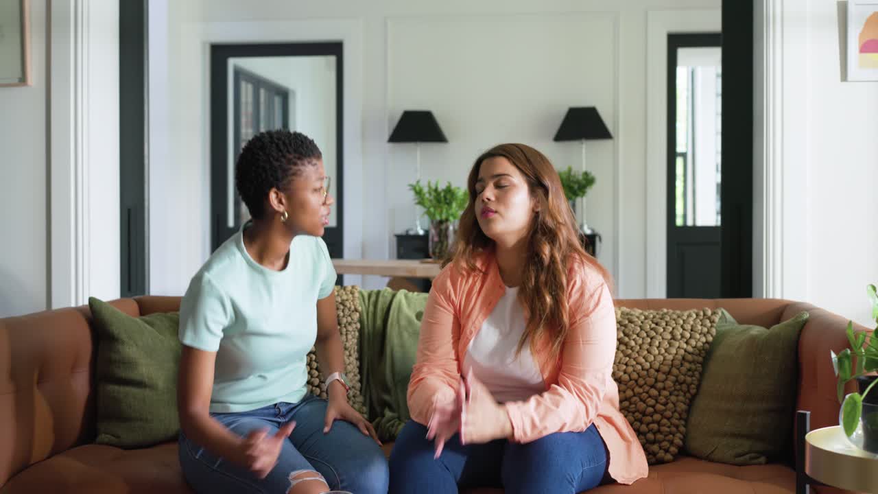 Diverse female friends on couch woman reading phone friend bringing pitcher and glasses comforting