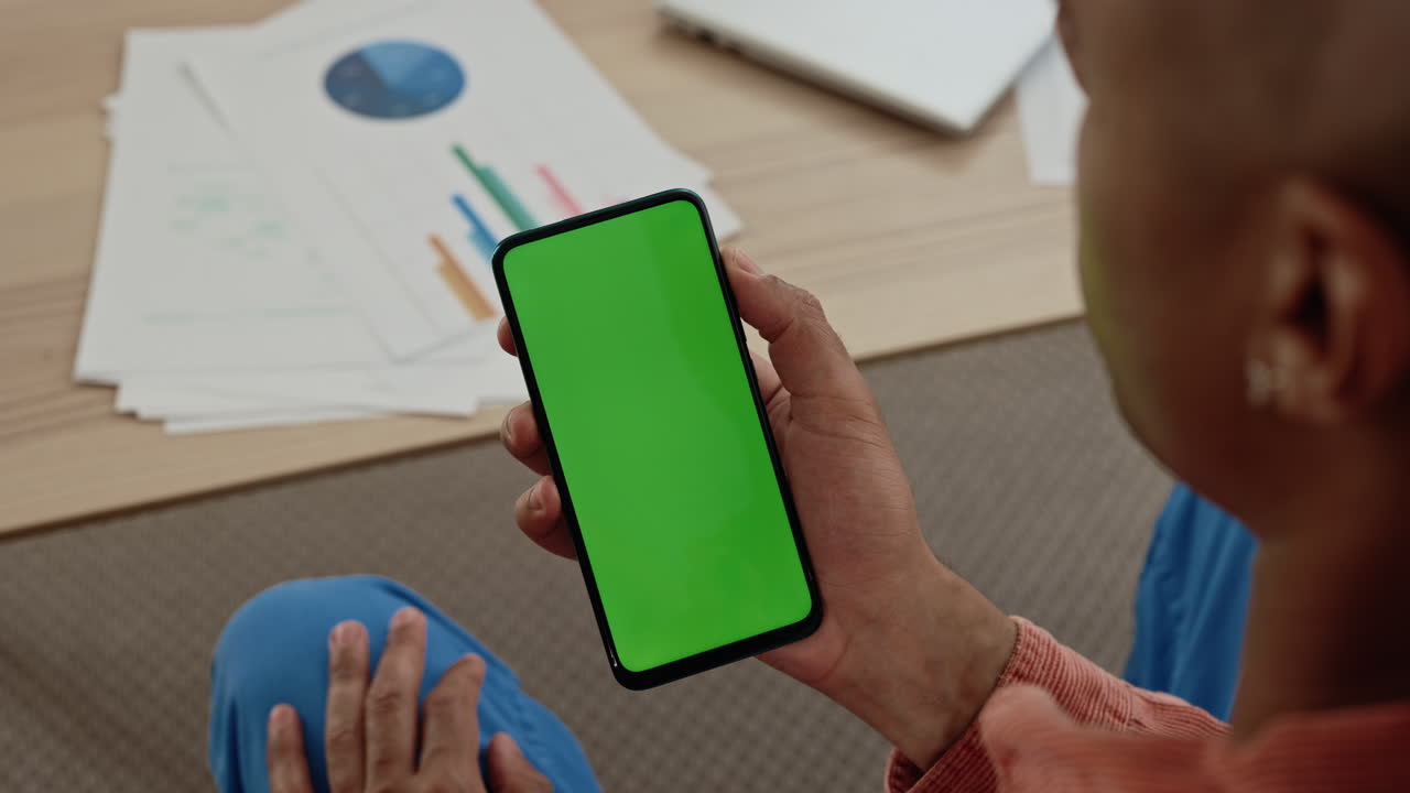 Person looking at a smartphone with a green screen in an office