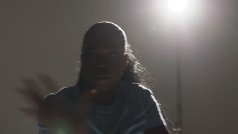 backlit head and shoulders studio portrait shot of young woman dancing in spotlight