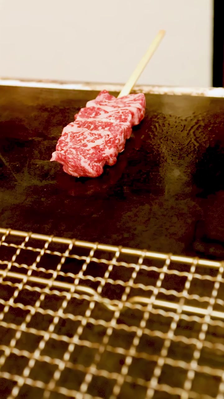Bidikan close-up sate daging sapi marmer mentah yang mendesis di atas panggangan panas di Osaka.