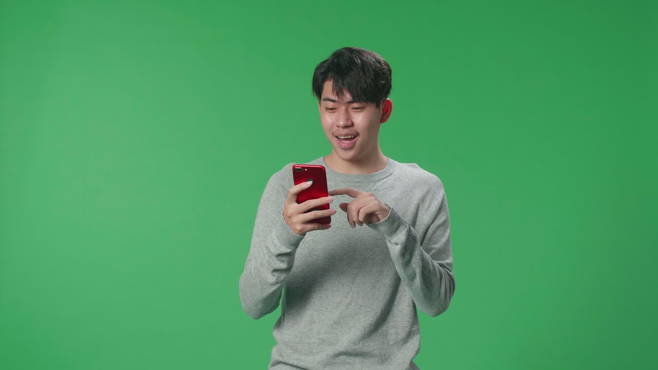 An Asian Man Enjoy Using Mobile Phone And Say Wow While Standing On Green Screen In The Studio