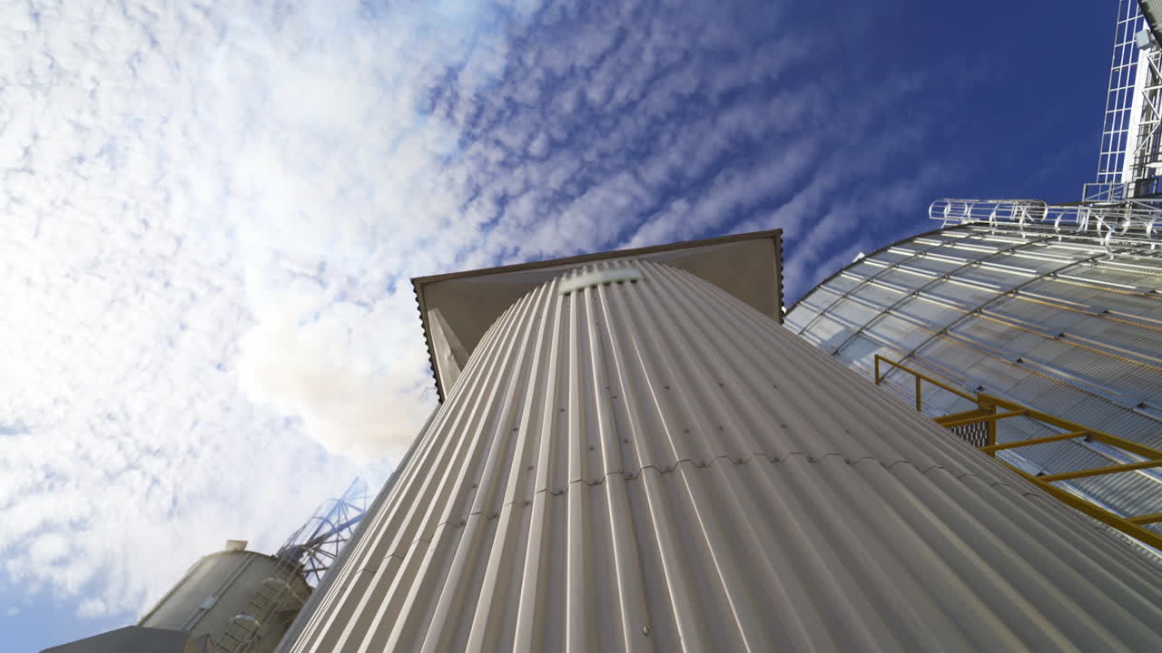 Metal grain elevator on sky background. Large granary for storing cereals. Thick smoke releasing into the air from industrial plant. Pollution. View from below.