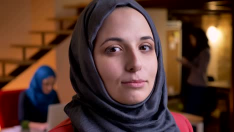 closeup portrait of young charming muslim female in gray hijab turning to camera and smiling cheerfully