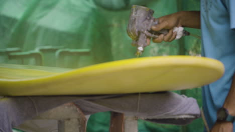 slow dolly right shot of shaper painting surfboard with paint sprayer