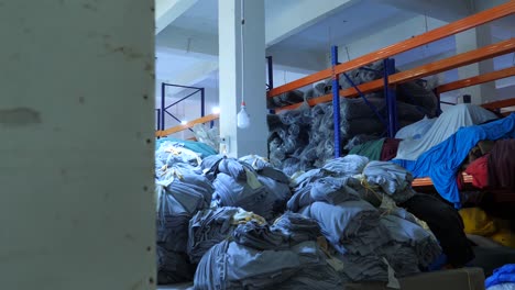 dolly reveal of storage room with rows of shelf racks full of fabric and piles of sacks, different cloth pieces and materials at clothing or shoe manufacturing factory