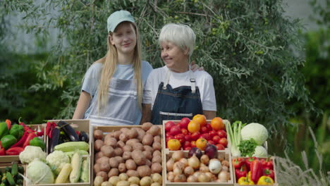 Retrato-De-Abuela-Y-Nieta-Felices-Paradas-Detrás-Del-Mostrador-De-Verduras-En-El-Mercado-De-Agricultores.