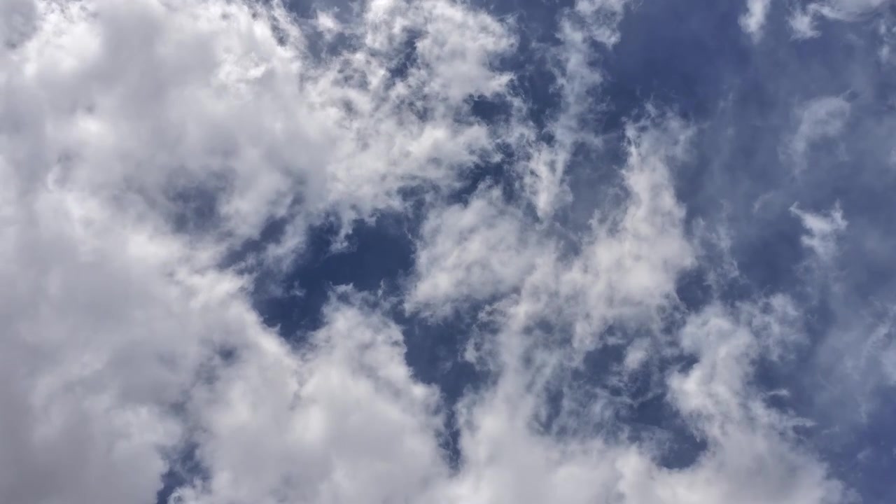 A cinematic drone timelapse captures fast moving overhead clouds passing swiftly across a blue sky. The rapid atmospheric motion creates a dynamic and evolving nature background.