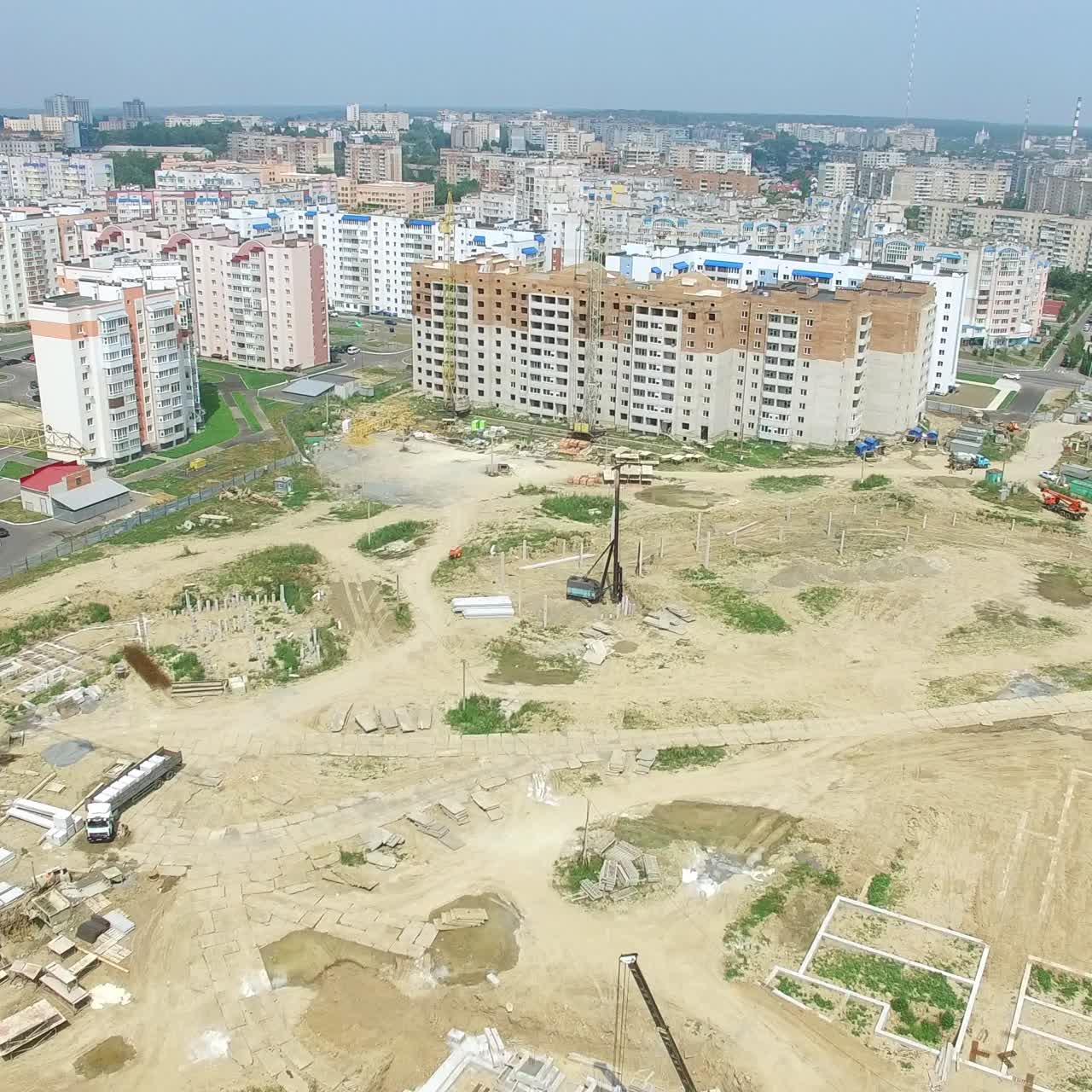 builders are working on the construction of a high-rise building in the city on the background of building materials, machinery and equipment. Aerial view