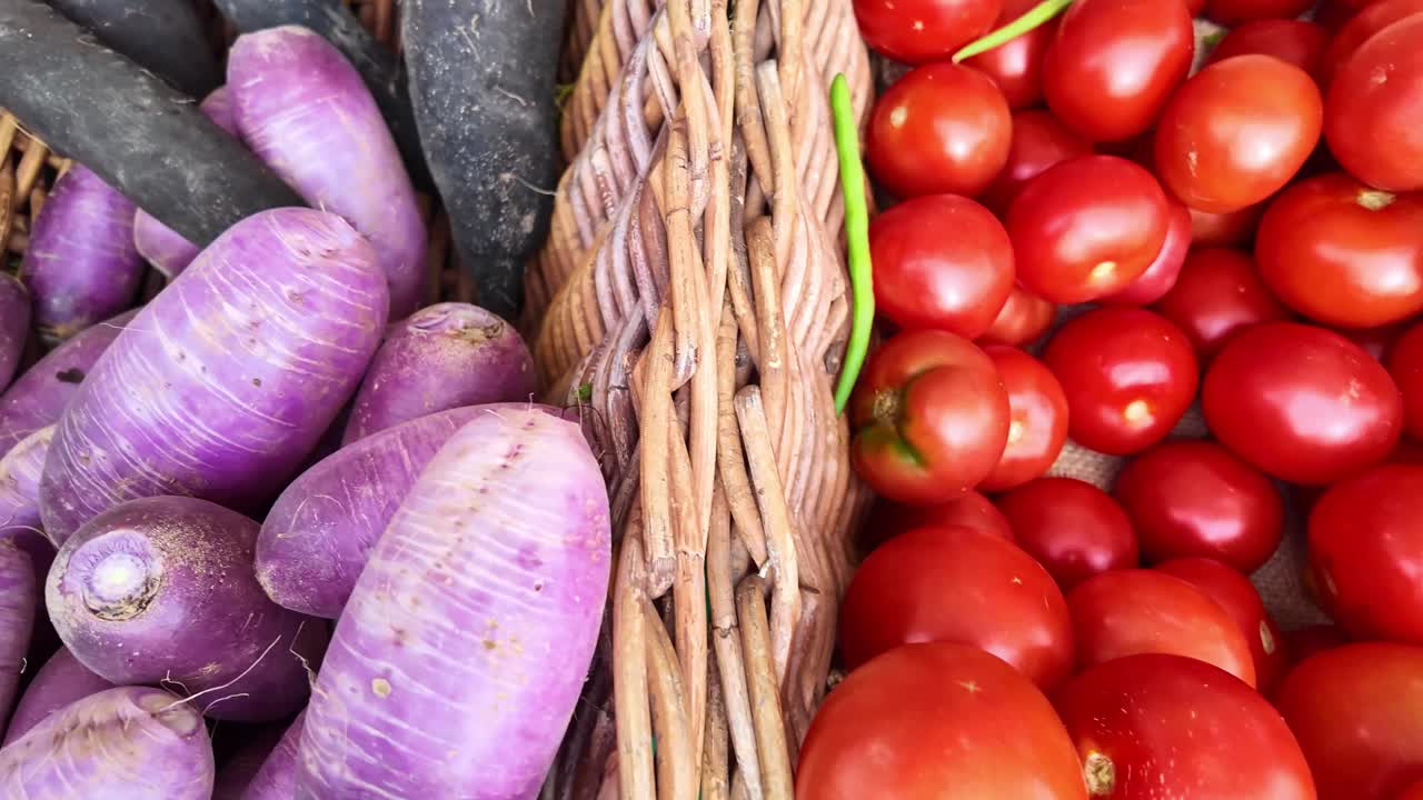 Top shot panning over tomatoes, purple radishes and black radish in wicker baskets