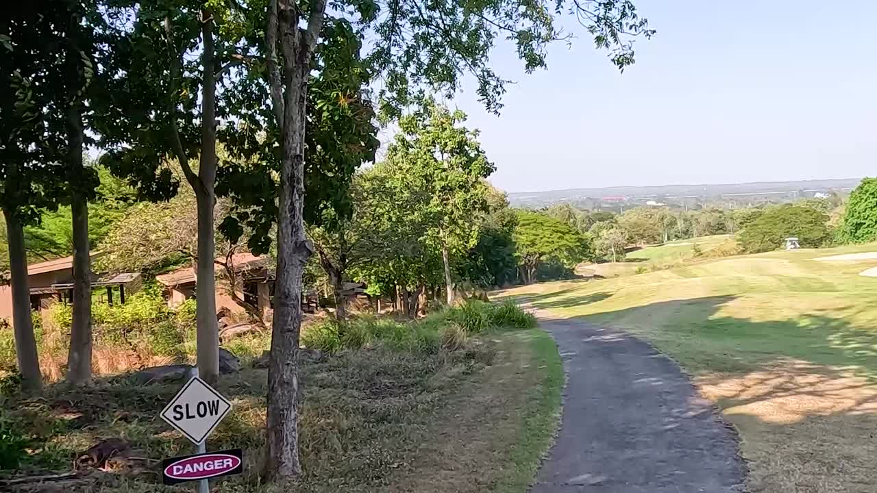 A serene pathway winds through a lush golf course, surrounded by trees and open green spaces under a clear sky.