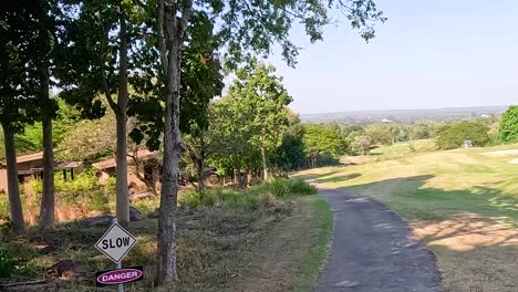 a serene pathway winds through a lush golf course, surrounded by trees and open green spaces under a clear sky.