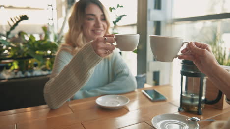 junge freundinnen, die mit tassen tee und kaffee anstoßen