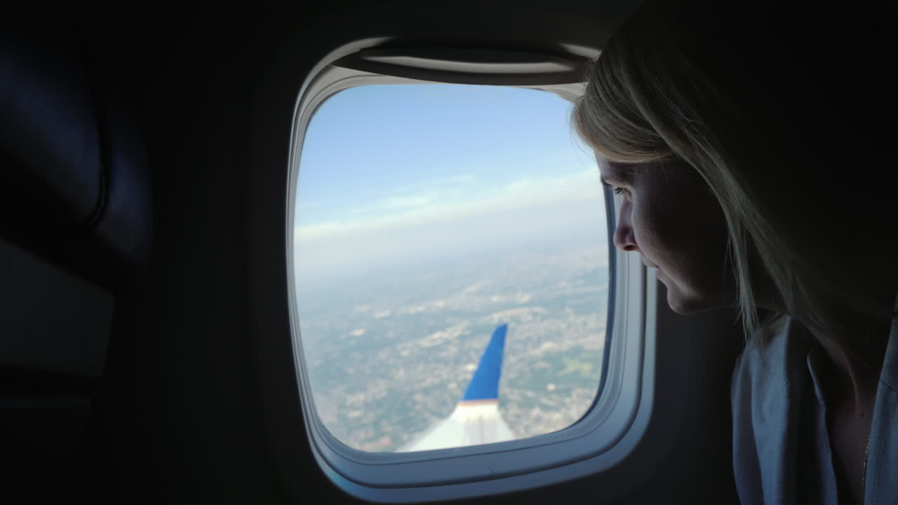 한 젊은 여성 승객이 비행기 창밖으로 미터기가 있는 곳 아래에 있는 땅을 바라보고 있습니다.