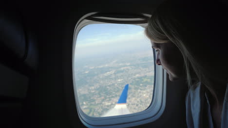 una joven pasajera mira por la ventana del avión hacia el suelo muy por debajo de donde está el metro