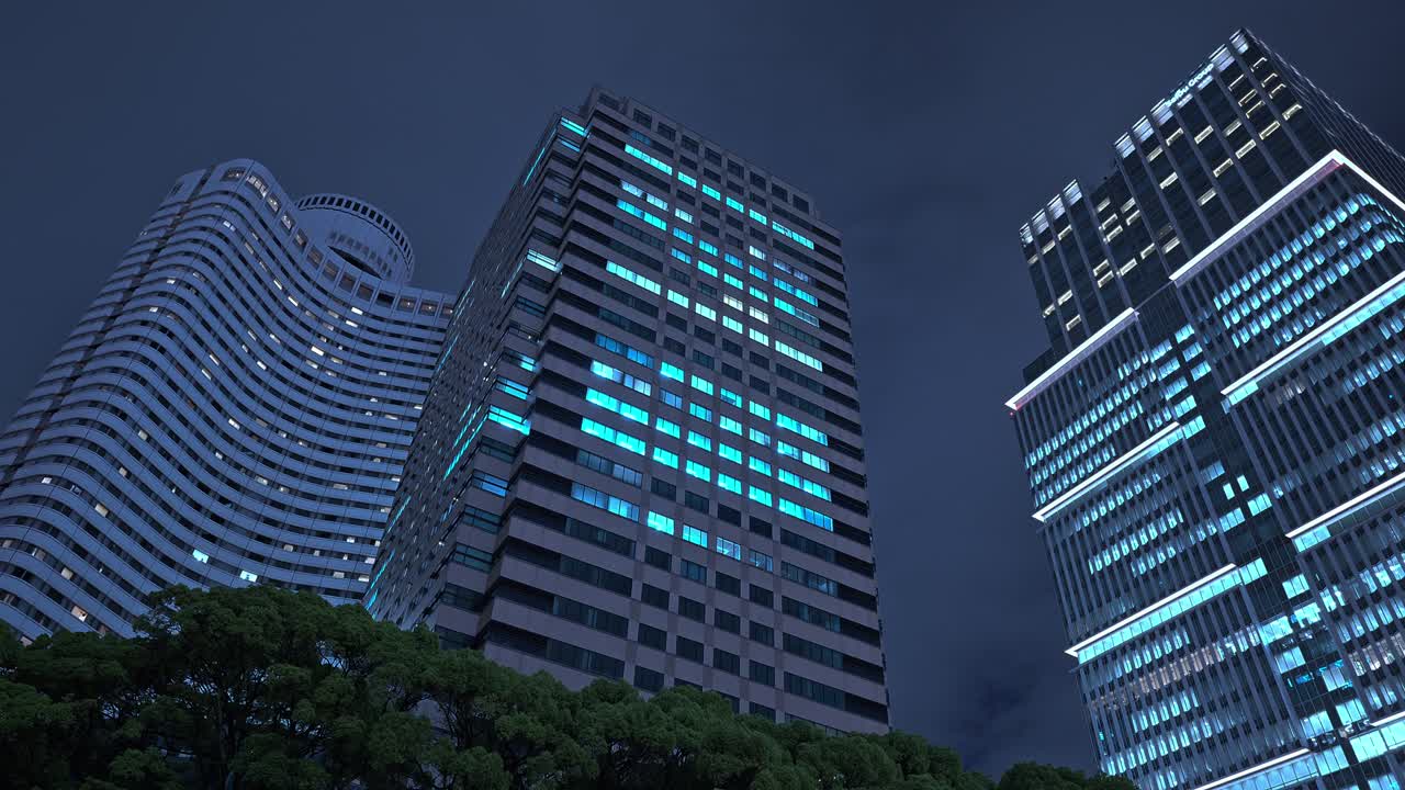Modern high-rise buildings in Akasaka-Mitsuke, Tokyo, illuminate the night sky with their glowing windows, showcasing the district's vibrant urban architecture after dark.