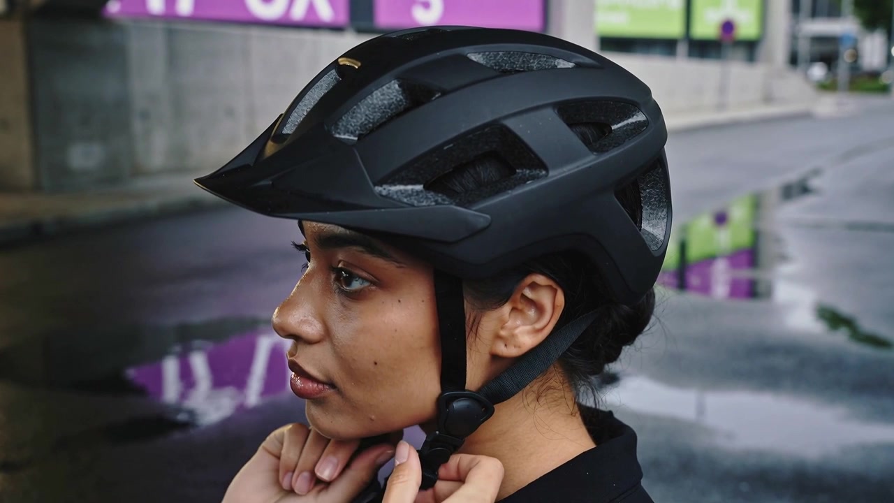 Una mano d'aiuto si protende, una donna stringe il sottogola del casco su una strada bagnata, preparandosi a partire.