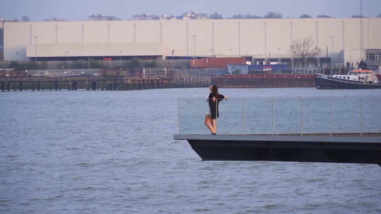 보트 부두 파도 주위를 비행하는 레일 울타리 머리에 그녀의 손을 쉬고 자유를 느끼기 위해 플랫폼의 가장자리로가는 물 바다로 둘러싸인 매력적인 여성