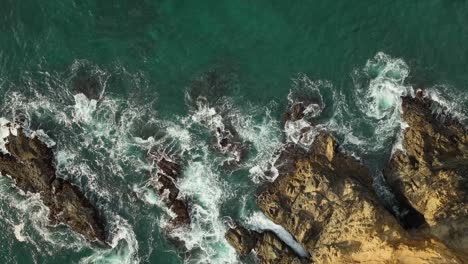 Top-down-view-of-waves-crashing-onto-a-rocky-coastline-in-the-Pacific-Ocean