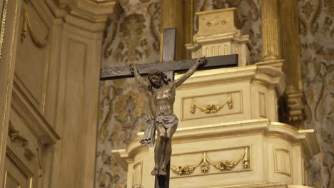 Crucifix-statue-of-Jesus-on-the-cross,-prominently-displayed-on-an-ornate-church-altar-with-intricate-gold-detailing