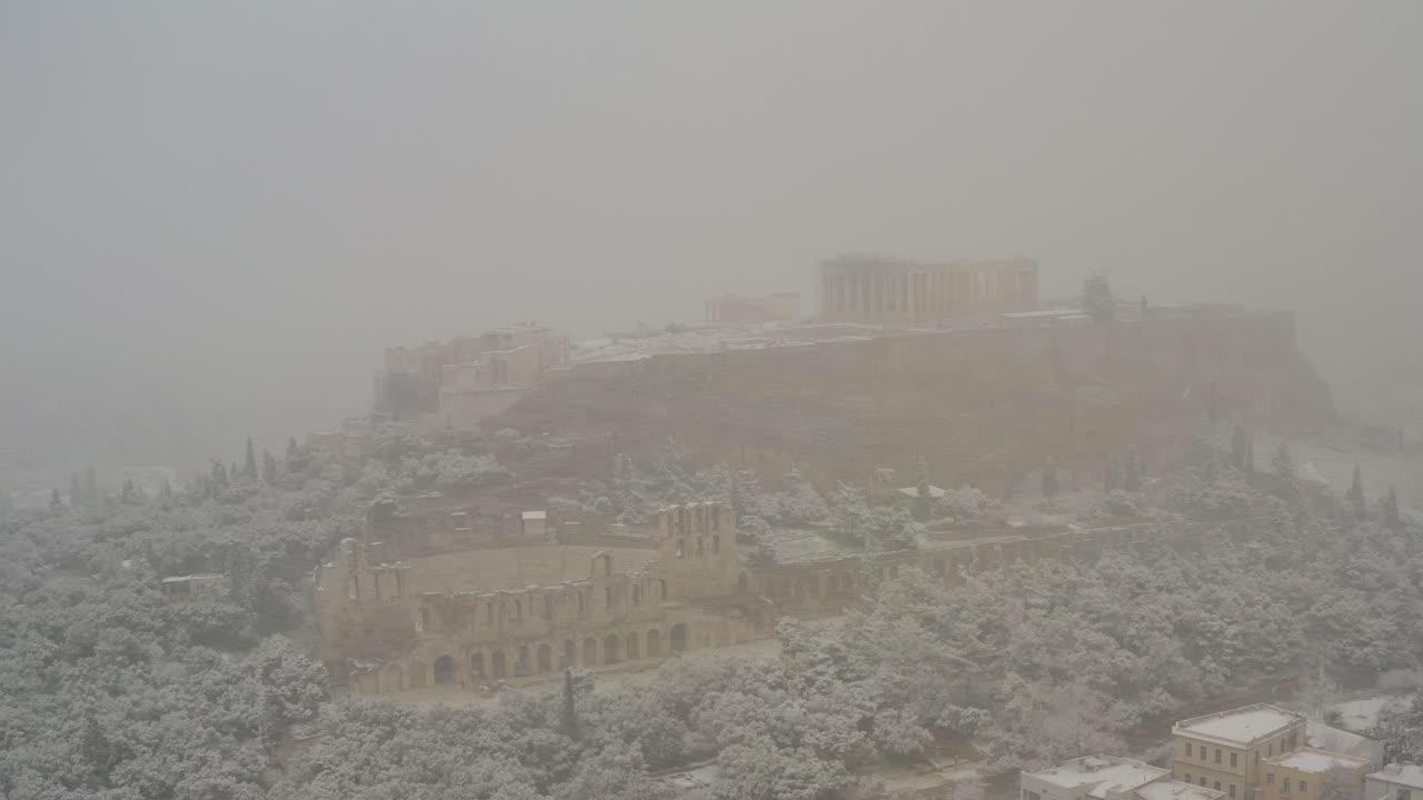 Vista aerea intorno alle rovine del Partenone coperte da fitta nebbia e neve, in un'insolita giornata invernale ad Atene, Grecia - inquadratura in orbita, con drone.