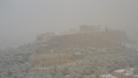 Aerial-view-around-the-Parthenon-ruins-covered-in-thick-fog-and-snow,-unusual-winter-day-in-Athens,-Greece---orbit,-drone-shot